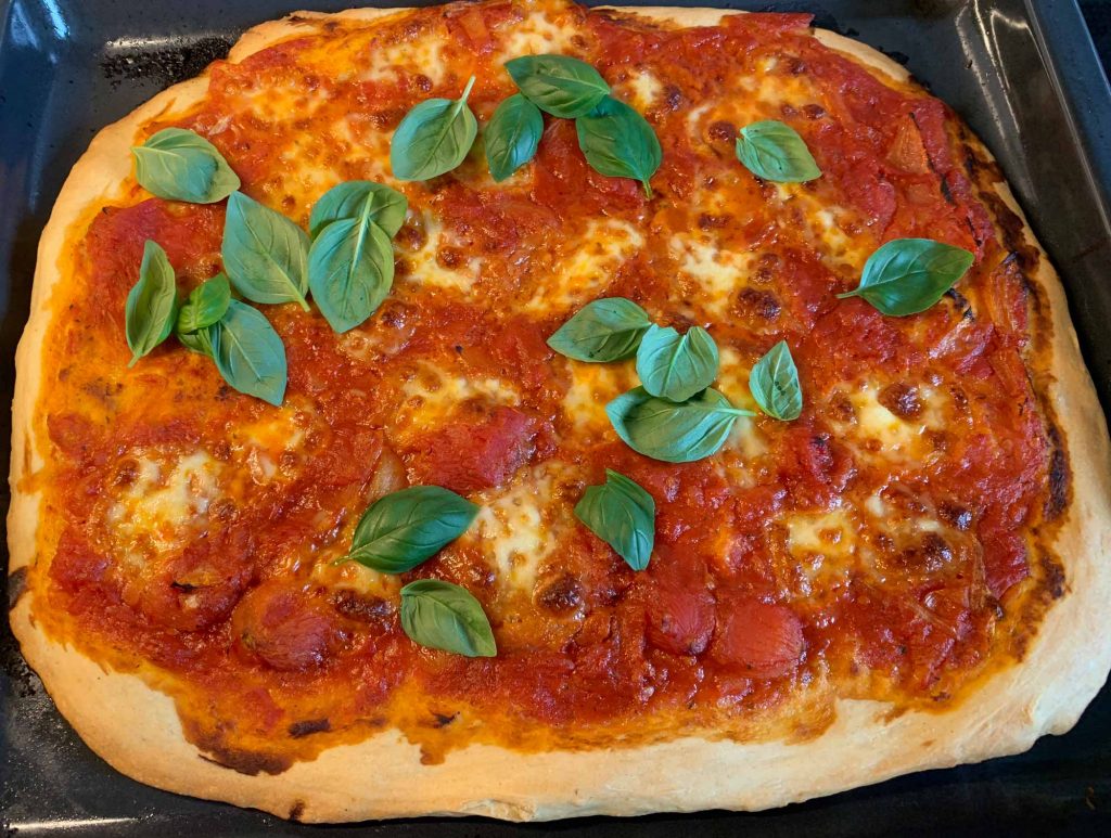 Pizza Margherita frisch aus dem Backofen, dekoriert mit frischem Basilikum, so wie es sein soll.