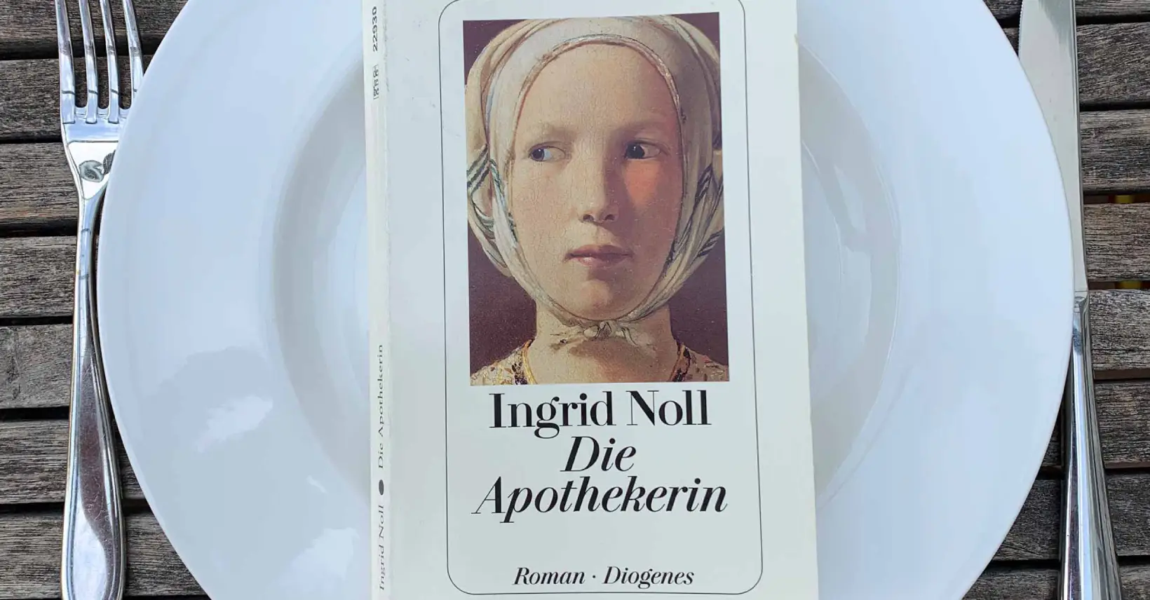 Der Roman „Die Apothekerin“ von Ingrid Noll liegt auf einem Teller, daneben das Messer und Gabel. Bereit zur Buchbesprechung?